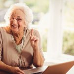 Smiling senior woman raising finger using laptop at home